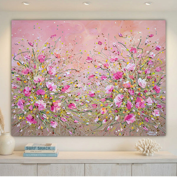 A large rectangular floral wall art painting hangs above a light console table. The artwork depicts pink flowers and branches with splashes of yellow, white, and green on a soft pink background.