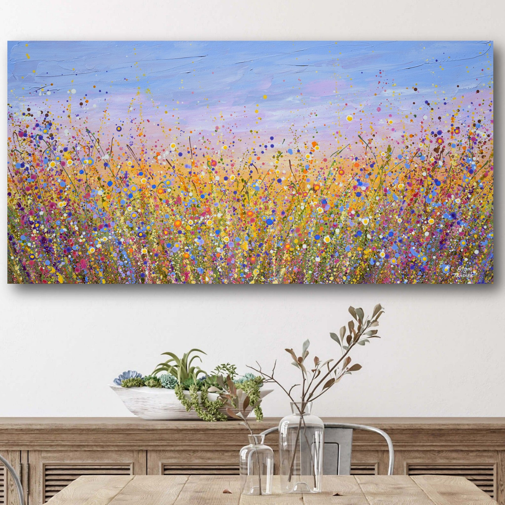 Colorful abstract painting of a field on a wall above a wooden table with decor items.